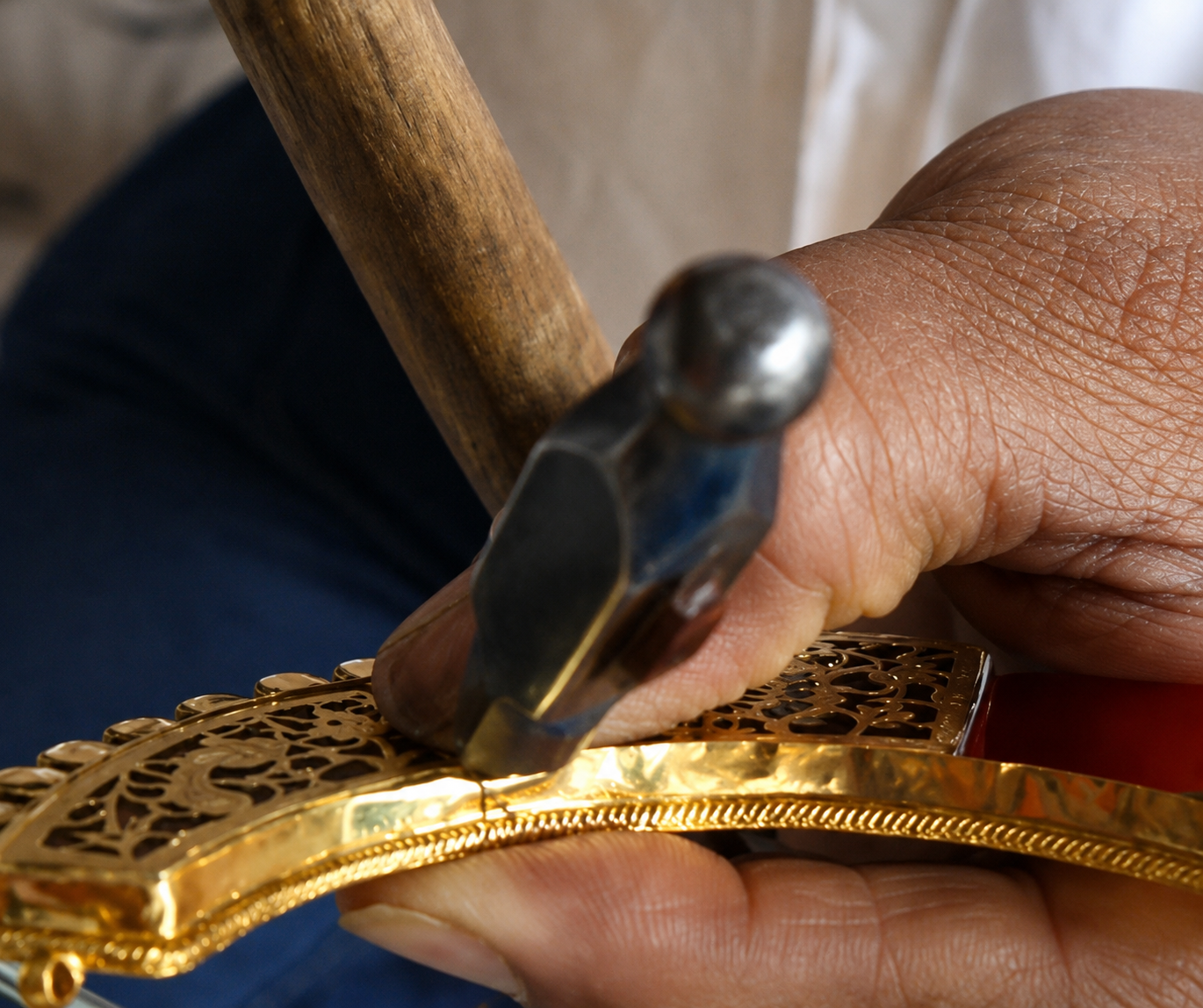 Jeweller using tweezers to set a cut stone ringed by small red stones into a jewellery piece held on a lac block